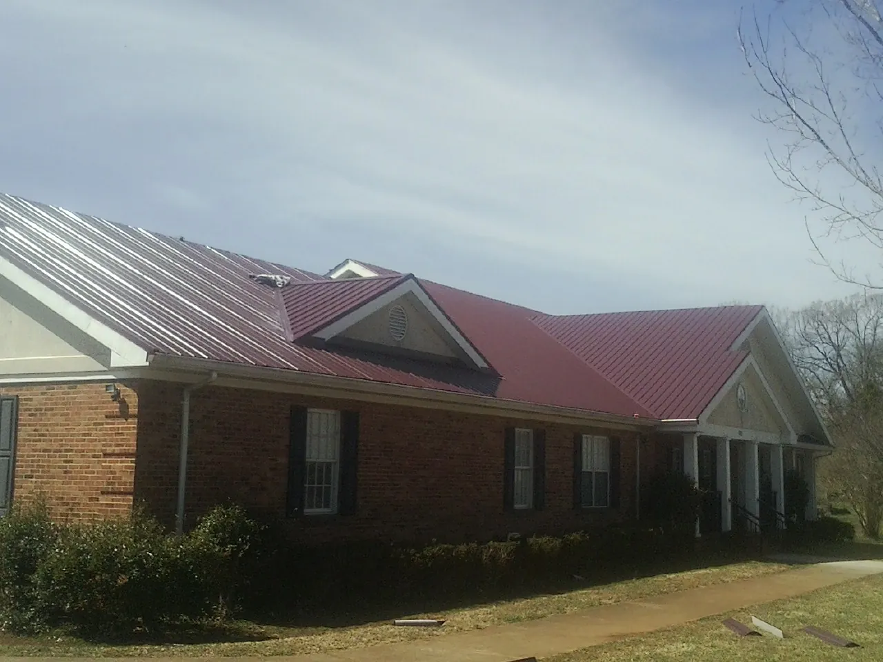 Red metal roof with gabled entries on a long brick building, from a Hail Damage Roof Repair job in Fork